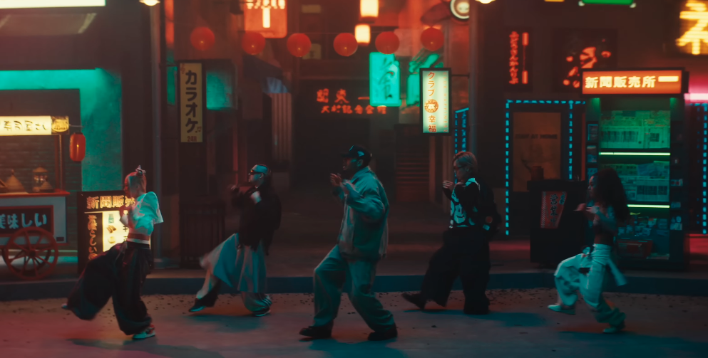 A screenshot of Chris Brown's Press Me video showing Chris Brown and four dancers in streetwear dance on a neon-lit street with Asian signage, capturing a vibrant urban nightlife scene. 